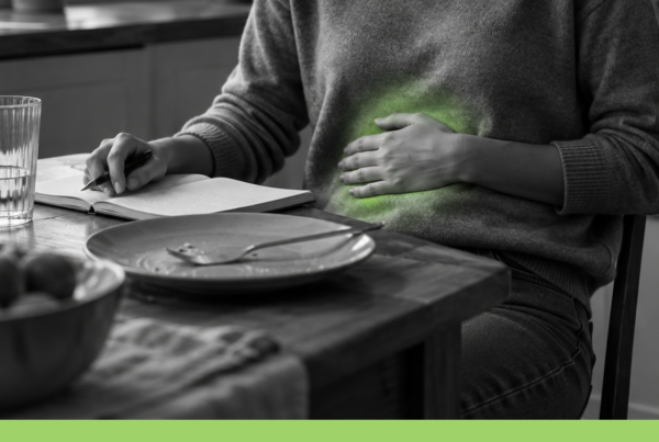 Persona seduta al tavolo dopo un pasto, con una mano sull’addome, taccuino aperto ed effetto neon verde illustrativo localizzato sulla pancia.