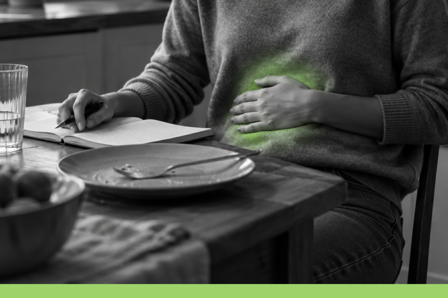 Persona seduta al tavolo dopo un pasto, con una mano sull’addome, taccuino aperto ed effetto neon verde illustrativo localizzato sulla pancia.
